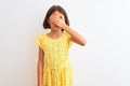 Young beautiful child girl wearing yellow floral dress standing over isolated white background covering eyes with hand, looking Royalty Free Stock Photo