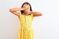 Young beautiful child girl wearing yellow floral dress standing over isolated white background Covering eyes and mouth with hands, Royalty Free Stock Photo