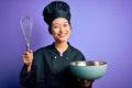 Young beautiful chinese chef woman wearing cooker uniform and hat using bowl and whisk with a happy face standing and smiling with Royalty Free Stock Photo