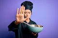 Young beautiful chinese chef woman wearing cooker uniform and hat using bowl and whisk with open hand doing stop sign with serious Royalty Free Stock Photo