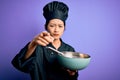 Young beautiful chinese chef woman wearing cooker uniform and hat using bowl and whisk pointing with finger to the camera and to Royalty Free Stock Photo