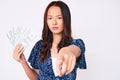 Young beautiful chinese girl holding dollars pointing with finger to the camera and to you, confident gesture looking serious Royalty Free Stock Photo