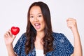 Young beautiful chinese girl holding heart screaming proud, celebrating victory and success very excited with raised arms Royalty Free Stock Photo
