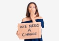 Young beautiful chinese girl holding we need a change banner covering mouth with hand, shocked and afraid for mistake