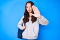 Young beautiful chinese girl holding student backpack with open hand doing stop sign with serious and confident expression,