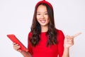 Young beautiful chinese girl holding touchpad smiling happy pointing with hand and finger to the side Royalty Free Stock Photo