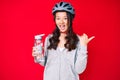 Young beautiful chinese girl wearing bike helmet and holding water bottle pointing thumb up to the side smiling happy with open Royalty Free Stock Photo