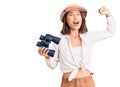 Young beautiful chinese girl wearing explorer hat holding binoculars screaming proud, celebrating victory and success very excited Royalty Free Stock Photo