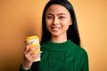 Young beautiful chinese woman drinking cup of coffee over isolated yellow background with a happy face standing and smiling with a Royalty Free Stock Photo