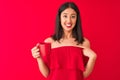 Young beautiful chinese woman drinking cup of coffee standing over isolated red background with surprise face pointing finger to Royalty Free Stock Photo