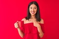 Young beautiful chinese woman drinking cup of coffee standing over isolated red background very happy pointing with hand and Royalty Free Stock Photo