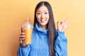 Young beautiful chinese woman drinking glass of orange juice doing ok sign with fingers, smiling friendly gesturing excellent Royalty Free Stock Photo