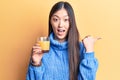 Young beautiful chinese woman drinking glass of orange juice pointing thumb up to the side smiling happy with open mouth Royalty Free Stock Photo