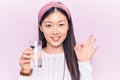 Young beautiful chinese woman drinking glass of water doing ok sign with fingers, smiling friendly gesturing excellent symbol