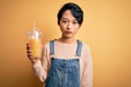 Young beautiful chinese woman drinking healthy orange juice over isolated yellow background with a confident expression on smart Royalty Free Stock Photo