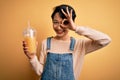 Young beautiful chinese woman drinking healthy orange juice over isolated yellow background with happy face smiling doing ok sign Royalty Free Stock Photo