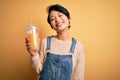 Young beautiful chinese woman drinking healthy orange juice over isolated yellow background with a happy face standing and smiling Royalty Free Stock Photo