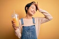 Young beautiful chinese woman drinking healthy orange juice over isolated yellow background stressed with hand on head, shocked Royalty Free Stock Photo