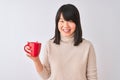 Young beautiful Chinese woman drinking red cup of coffee over isolated white background with a happy face standing and smiling Royalty Free Stock Photo