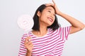 Young beautiful chinese woman eating lollipop standing over isolated white background stressed with hand on head, shocked with Royalty Free Stock Photo