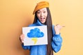 Young beautiful chinese woman holdig cloud and thunder draw pointing thumb up to the side smiling happy with open mouth