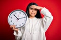 Young beautiful chinese woman holding big clock standing over isolated red background stressed with hand on head, shocked with Royalty Free Stock Photo