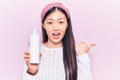 Young beautiful chinese woman holding bottle with cream lotion pointing thumb up to the side smiling happy with open mouth Royalty Free Stock Photo