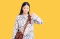Young beautiful chinese woman holding briefcase with angry face, negative sign showing dislike with thumbs down, rejection concept
