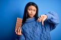 Young beautiful chinese woman holding chocolate bar over isolated blue background with angry face, negative sign showing dislike Royalty Free Stock Photo