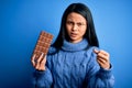 Young beautiful chinese woman holding chocolate bar over isolated blue background annoyed and frustrated shouting with anger, Royalty Free Stock Photo