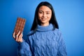 Young beautiful chinese woman holding chocolate bar over isolated blue background with a happy face standing and smiling with a Royalty Free Stock Photo