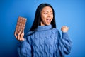 Young beautiful chinese woman holding chocolate bar over isolated blue background pointing and showing with thumb up to the side Royalty Free Stock Photo