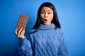 Young beautiful chinese woman holding chocolate bar over isolated blue background scared in shock with a surprise face, afraid and Royalty Free Stock Photo
