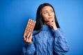 Young beautiful chinese woman holding chocolate bar over isolated blue background serious face thinking about question, very Royalty Free Stock Photo