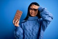 Young beautiful chinese woman holding chocolate bar over isolated blue background stressed with hand on head, shocked with shame Royalty Free Stock Photo