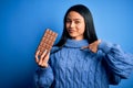 Young beautiful chinese woman holding chocolate bar over isolated blue background with surprise face pointing finger to himself Royalty Free Stock Photo