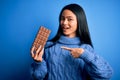 Young beautiful chinese woman holding chocolate bar over isolated blue background very happy pointing with hand and finger Royalty Free Stock Photo