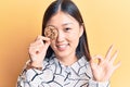 Young beautiful chinese woman holding cookie over eye doing ok sign with fingers, smiling friendly gesturing excellent symbol