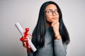 Young beautiful chinese woman holding diploma standing over isolated white background serious face thinking about question, very Royalty Free Stock Photo