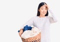 Young beautiful chinese woman holding laundry basket with clothes stressed and frustrated with hand on head, surprised and angry Royalty Free Stock Photo
