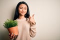 Young beautiful chinese woman holding plant pot standing over isolated white background happy with big smile doing ok sign, thumb Royalty Free Stock Photo