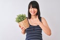 Young beautiful Chinese woman holding plant pot standing over isolated white background happy with big smile doing ok sign, thumb Royalty Free Stock Photo