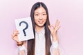 Young beautiful chinese woman holding question mark doing ok sign with fingers, smiling friendly gesturing excellent symbol