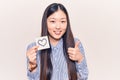 Young beautiful chinese woman holding reminder with heart shape smiling happy and positive, thumb up doing excellent and approval