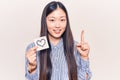 Young beautiful chinese woman holding reminder with heart shape smiling with an idea or question pointing finger with happy face,