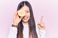 Young beautiful chinese woman holding slice of lemon over eye smiling with an idea or question pointing finger with happy face,