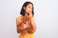 Young beautiful chinese woman holding teddy bear standing over isolated white background cover mouth with hand shocked with shame Royalty Free Stock Photo