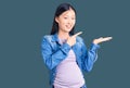 Young beautiful chinese woman pregnant expecting baby amazed and smiling to the camera while presenting with hand and pointing