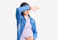 Young beautiful chinese woman pregnant expecting baby covering eyes with arm, looking serious and sad