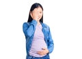 Young beautiful chinese woman pregnant expecting baby covering one eye with hand, confident smile on face and surprise emotion
